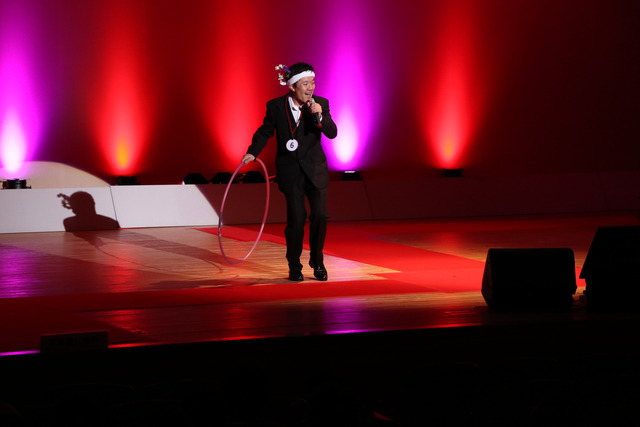 双葉ふれあい文化館にて舞台の上で男性の方がフラフープを持ちながら歌っている写真